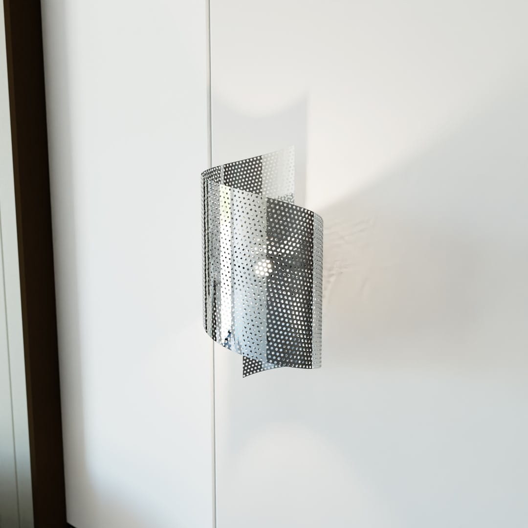 Chromowany kinkiet Spiral 1xG9 w srebrnym kolorze, o falistym kształcie z perforowaną powierzchnią, montowany na ścianie. Widoczny detal światła wewnętrznego, na tle gładkiej, białej ściany.