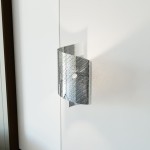 Chromowany kinkiet Spiral 1xG9 w srebrnym kolorze, o falistym kształcie z perforowaną powierzchnią, montowany na ścianie. Widoczny detal światła wewnętrznego, na tle gładkiej, białej ściany.