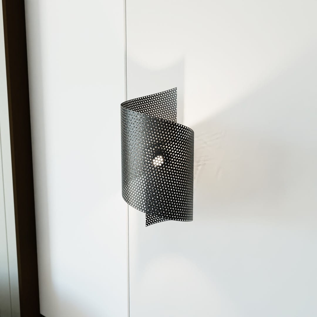 Spiral black kinkiet 1xG9 w kolorze czarnym, wykonany z perforowanego metalu, zamontowany na ścianie. Kinkiet ma lekko falowany kształt i centralny punkt świetlny, emitujący światło przez otwory w obudowie. Tło białe, minimalistyczne.