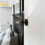 Czarny kinkiet Spiral 1xG9 z perforowaną, falistą osłoną, zamontowany na białej ścianie. Widoczna metalowa podstawka i subtelne światło emitowane przez żarówkę. Kinkiet w nowoczesnym stylu, idealny do aranżacji wnętrz.