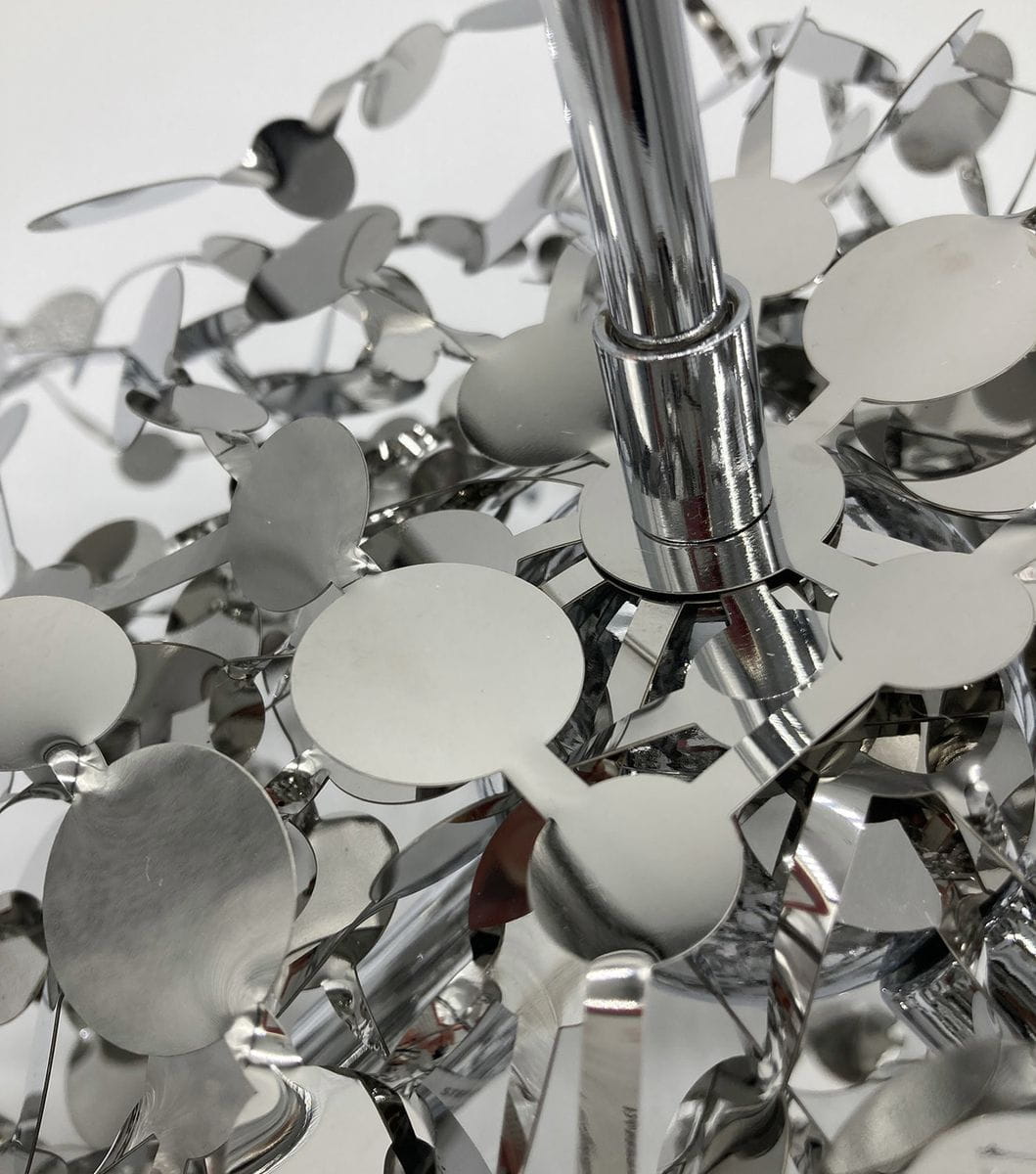 Lampa wisząca Monetti w kolorze chromu, z trzema oprawkami G9. Widoczne metalowe, błyszczące okręgi tworzące dekoracyjny wzór, z centralnym elementem montażowym. Zbliżenie na detale konstrukcji lampy.