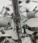 Lampa wisząca Monetti z chromowanym wykończeniem, z trzema miejscami na żarówki G9. Widok z bliska na detal mocowania oraz metalowe elementy w kształcie okręgów i figury, tworzące dekoracyjny wzór. Tło proste, białe.