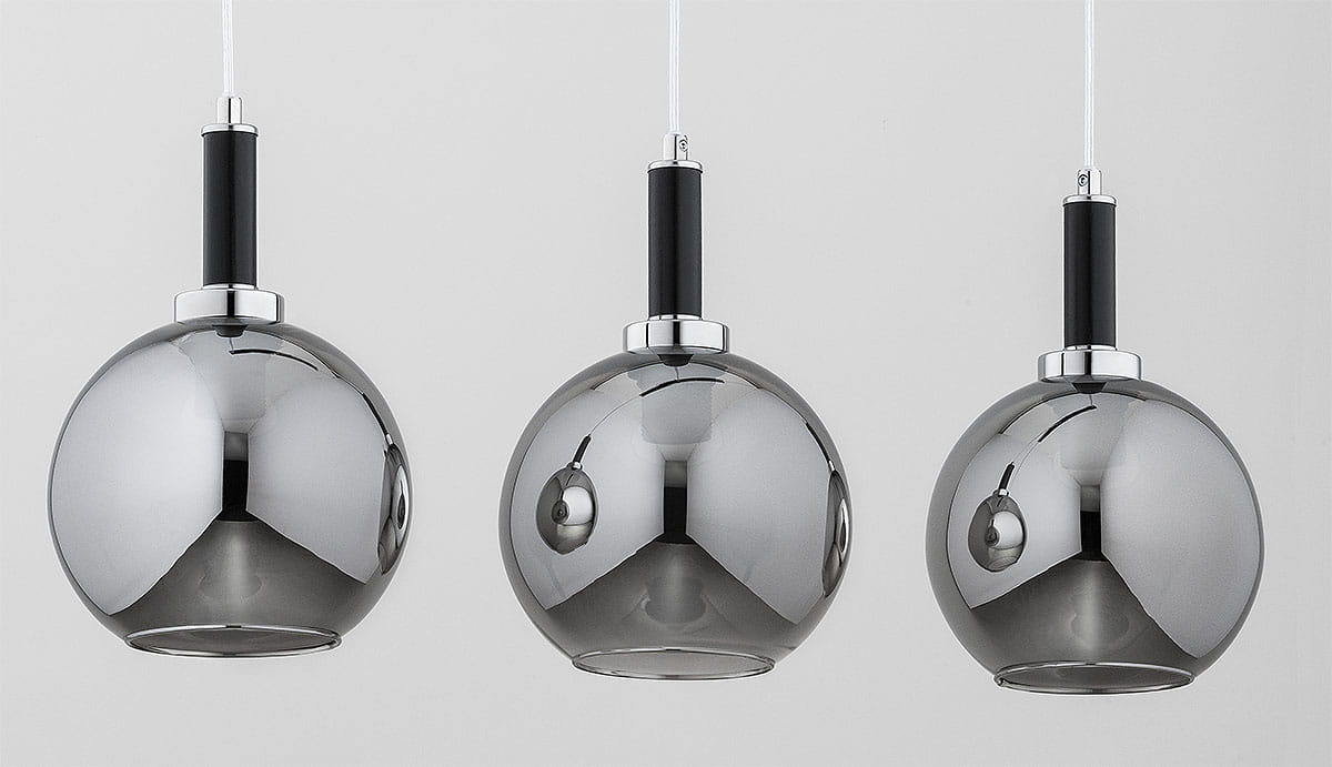 Lampa wisząca Hetty w kolorze czarnym i chromowanym, składająca się z trzech okrągłych kloszy z metalicznym wykończeniem. Klosze zawieszone na białych przewodach, z czarnymi uchwytami. Ujęcie frontalne, zbliżenie na detale.