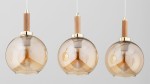 Lampa wisząca Hetty z trzema kloszami w kształcie kul, w kolorze złotym z drewnianymi elementami. Klosze wykonane z przezroczystego szkła w odcieniu brązowym, z widocznymi żarówkami E27. Ujęcie frontalne, lampy zawieszone na białych przewodach.