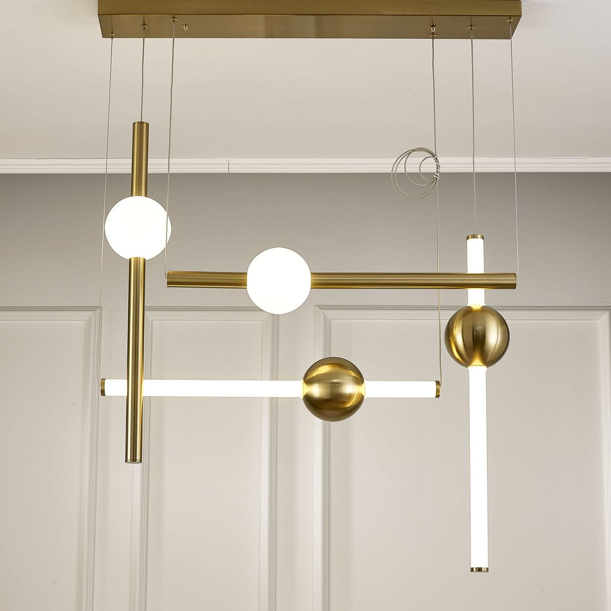 Lampa wisząca O-line L-4 w kolorze mosiężnym z czterema źródłami LED. Składa się z różnych elementów: kul, prostokątów i rur, zawieszonych na cienkich linkach. Produkt ma nowoczesny design, idealny do aranżacji wnętrz.