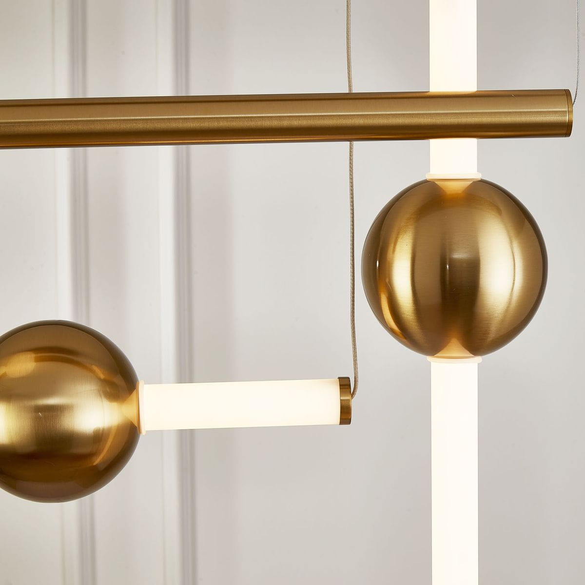 Lampa wisząca O-line L-4 z czterema źródłami LED, wykonana z mosiądzu. Elementy w formie kul i prostokątnych rur, w kolorze złotym, z białymi kloszami LED. Zbliżenie na detale konstrukcji i wykończenia.
