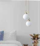 Lampa wisząca Pearl z jedną oprawą E27, złota, z białą szklaną kulą. Zawieszona na cienkim kablu, umieszczona w jasnym wnętrzu sypialni z białą pościelą i rośliną w doniczce. Kąt ujęcia frontalny, ukazuje lampę w kontekście aranżacji.