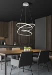 Lampa wisząca Bologna LED 1-punktowa w kolorze chromu, złożona z dwóch spiralnych pierścieni. Zawieszona na cienkich kablach w nowoczesnej aranżacji kuchni, nad drewnianym stołem z szarymi krzesłami i roślinami. Ciemne tło podkreśla elegancję lampy.