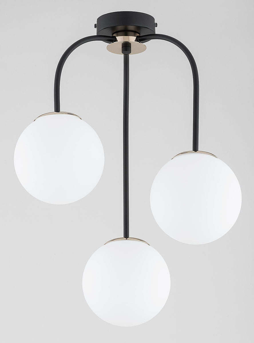 Lampa sufitowa Gamma z trzema kulistymi kloszami w białym kolorze, zawieszona na czarnych metalowych ramionach. Elementy złote przy mocowaniu. Ujęcie frontalne, pokazujące całą konstrukcję w minimalistycznym stylu.