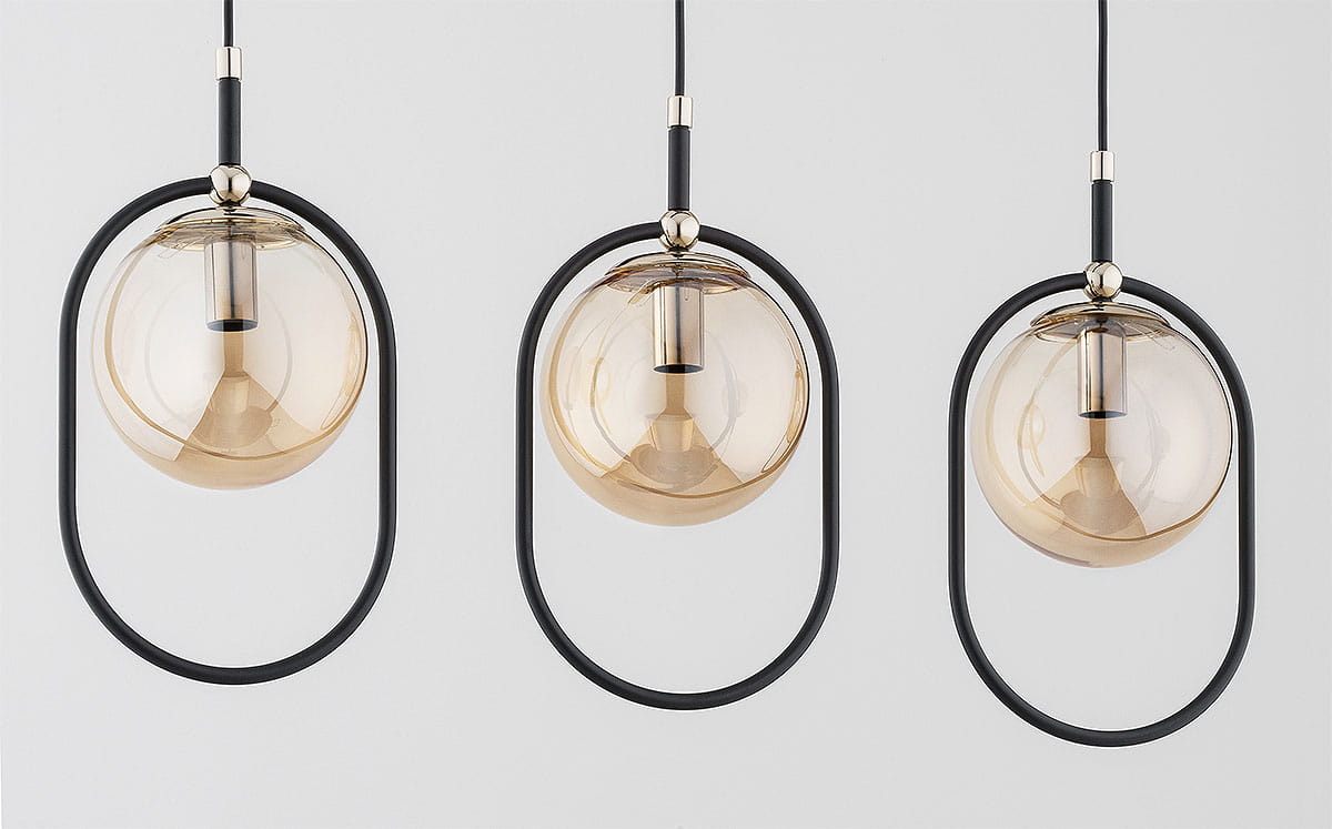 Lampa wisząca Amaro 3xE14 w kolorze czarnym i złotym. Posiada trzy szklane klosze w kształcie kul, zawieszone na czarnych metalowych obręczach. Ujęcie frontalne, klosze w przezroczystym odcieniu złota, z widocznymi oprawkami.