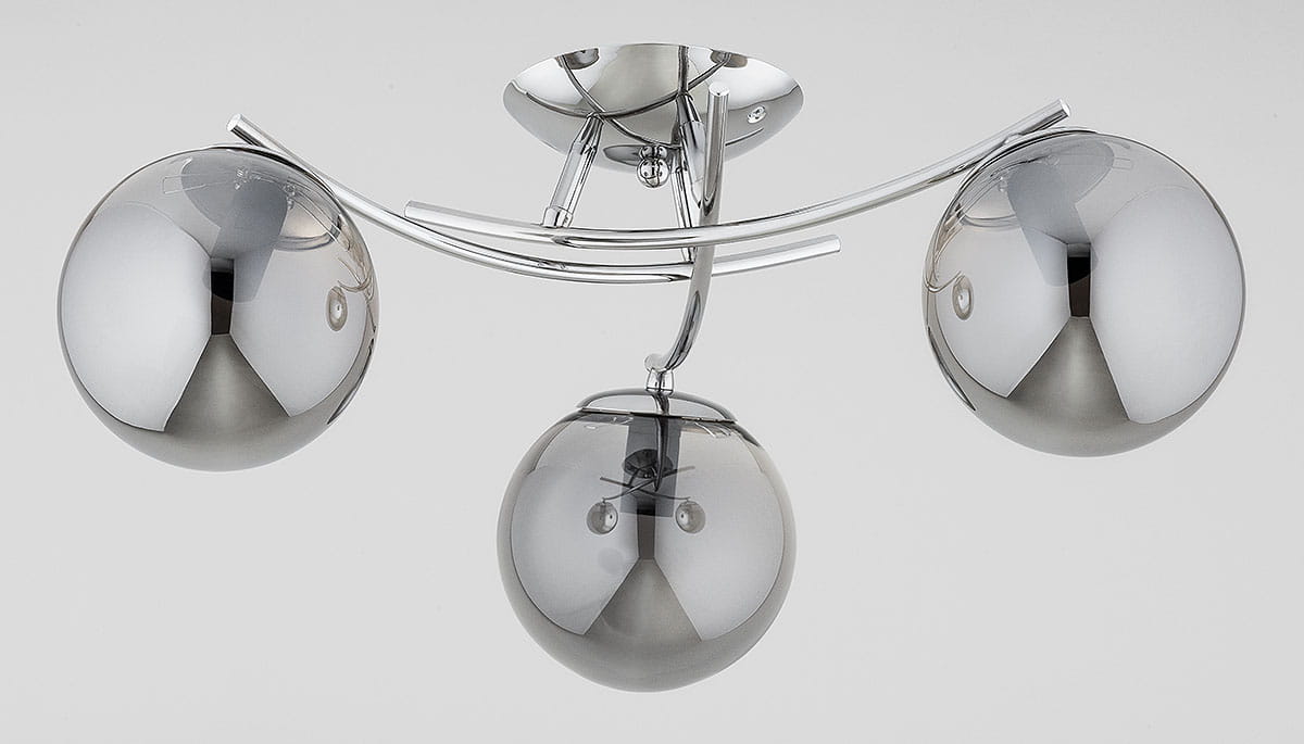 Lampa sufitowa Savi z trzema oprawami E14 w chromowanej obudowie. Szklane klosze w kolorze ciemnego srebra, okrągłe, umieszczone na metalowych ramionach. Ujęcie z przodu, pokazujące detal designu i połyskujące wykończenie.