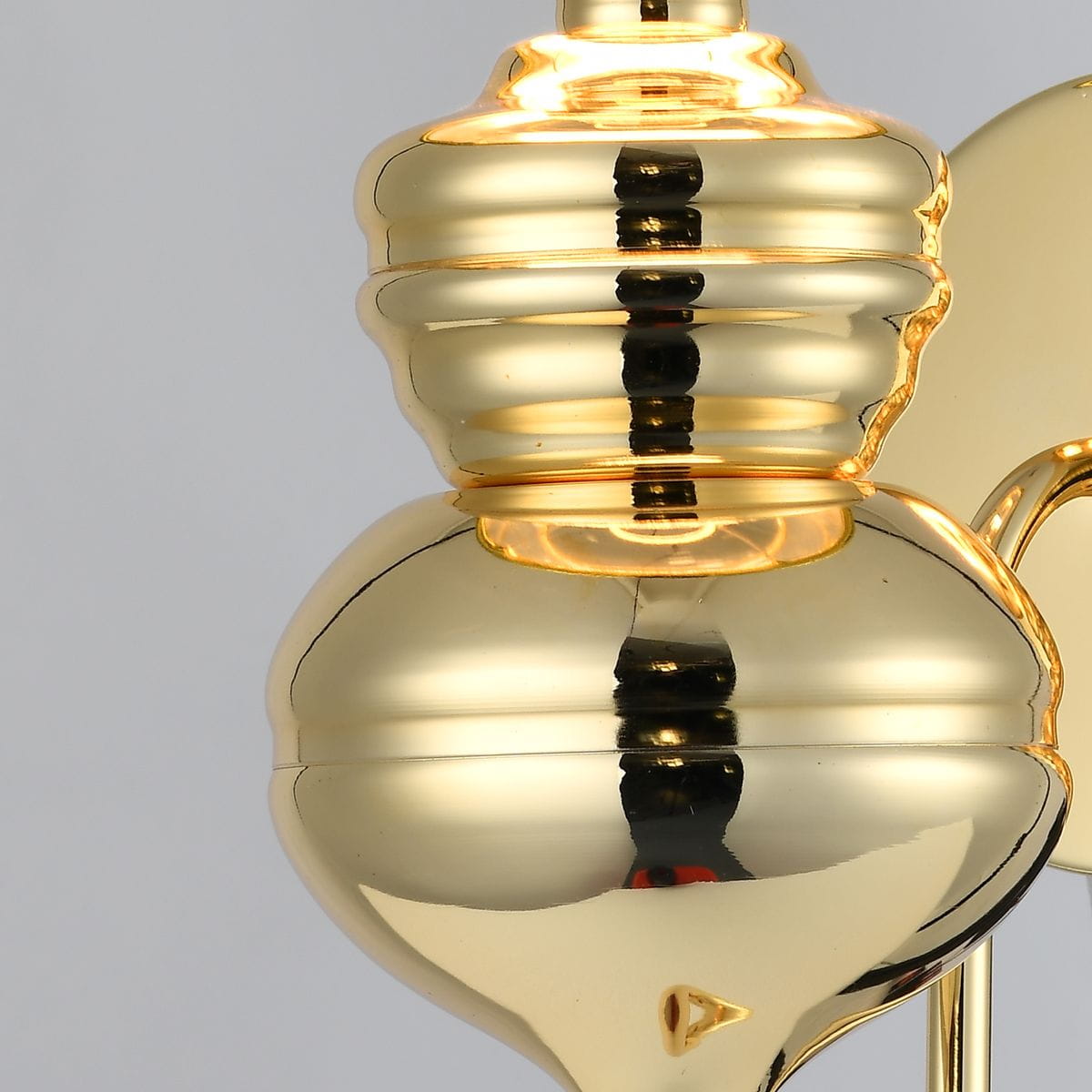 Kinkiet Queen D25 w kolorze złotym, z ceramiczną podstawą o zaokrąglonym kształcie, widocznymi detalami w formie pierścieni. Ujęcie z bliska na górną część lampy, z refleksami światła na błyszczącej powierzchni. Wymaga żarówki E27.