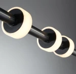 Lampa wisząca Ringo w kolorze czarnym, z trzema okrągłymi kloszami wykonanymi z mlecznego materiału, umieszczona na metalowym ramieniu. Klosze mają ciemne wykończenie od spodu, a całość montowana jest na gładkim tle.