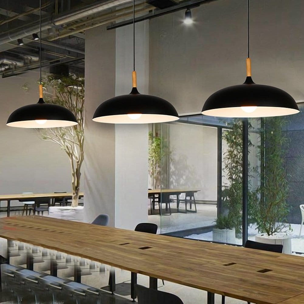 Lampa wisząca Saucer 1xE27 w kolorze czarnym, z metalowym kloszem i drewnianym uchwytem. Zawieszona w nowoczesnej przestrzeni biurowej nad drewnianym stołem, w otoczeniu roślinności.