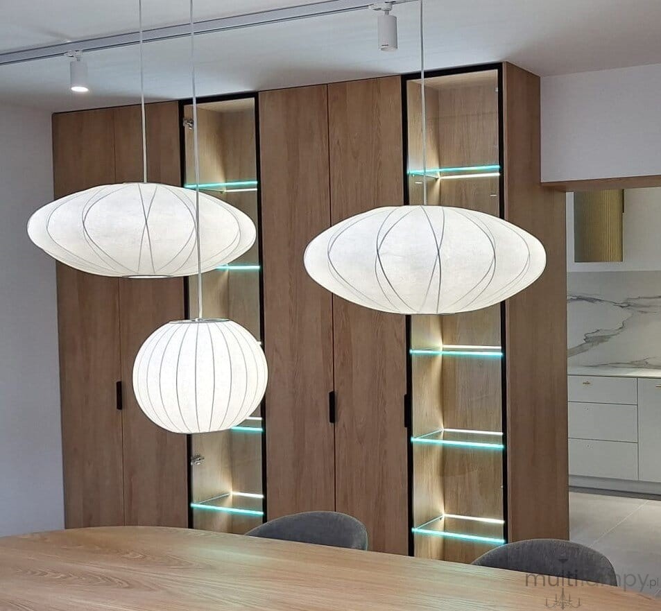 Lampa wisząca Silk D30 w białym kolorze, z jedną oprawą E27, w kształcie owalu i kuli. Zawieszona nad drewnianym stołem, obok nowoczesnych mebli z podświetleniem LED w tle.