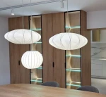 Lampa wisząca Silk D30 w białym kolorze, z jedną oprawą E27, w kształcie owalu i kuli. Zawieszona nad drewnianym stołem, obok nowoczesnych mebli z podświetleniem LED w tle.