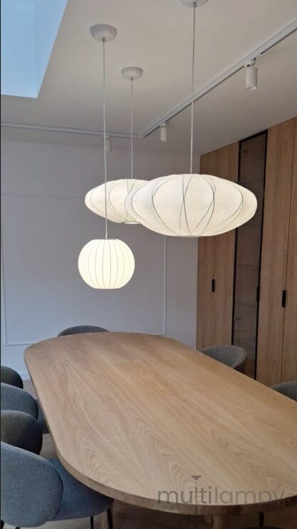 Lampa wisząca Silk D30 w białym kolorze, z jedną żarówką E27, zawieszona w kuchni nad drewnianym stołem. W zestawie owalne i kuliste klosze o teksturowanej powierzchni, z cienkimi liniami dekoracyjnymi. Tło jasne, minimalistyczne wnętrze.