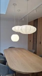 Lampa wisząca Silk D40 w białym kolorze z trzema kloszami o różnych kształtach, zawieszona nad drewnianym stołem. Klosze mają delikatne wzory i są umieszczone na prostych, białych przewodach w jasnym wnętrzu.
