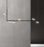 Lampa wisząca Simply z sześcioma oprawami G9, w kolorze czarnym. Konstrukcja składająca się z prostokątnej metalowej ramy z przezroczystymi szklanymi kulami, zawieszona poziomo na tle szarej ściany.