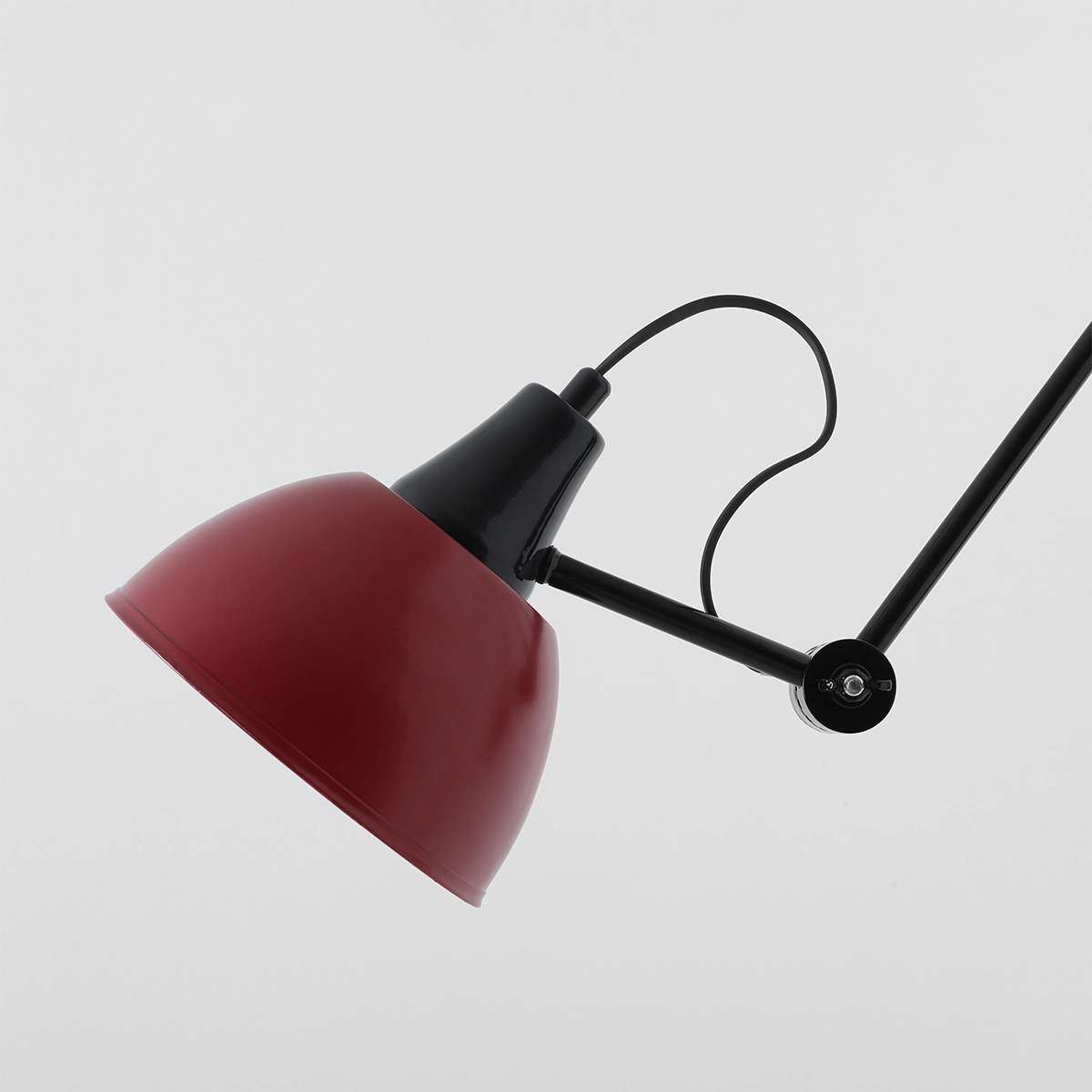 Lampa wisząca Aida z metalowym kloszem w kolorze czerwonym i czarnym ramieniem. Ujęcie z boku, pokazujące kształt klosza oraz detal mocowania. Idealna do nowoczesnych wnętrz, wykorzystująca żarówkę E27.