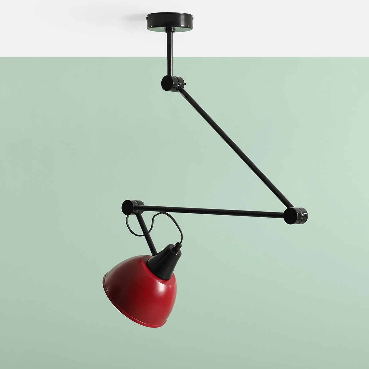 Lampa wisząca Aida z jedną oprawą E27 w kolorze czarnym i czerwonym. Zawieszona na regulowanym ramieniu, z czerwonym kloszem w kształcie stożka i czarnym elementem mocującym. Ujęcie z boku na jednolitym zielonym tle.