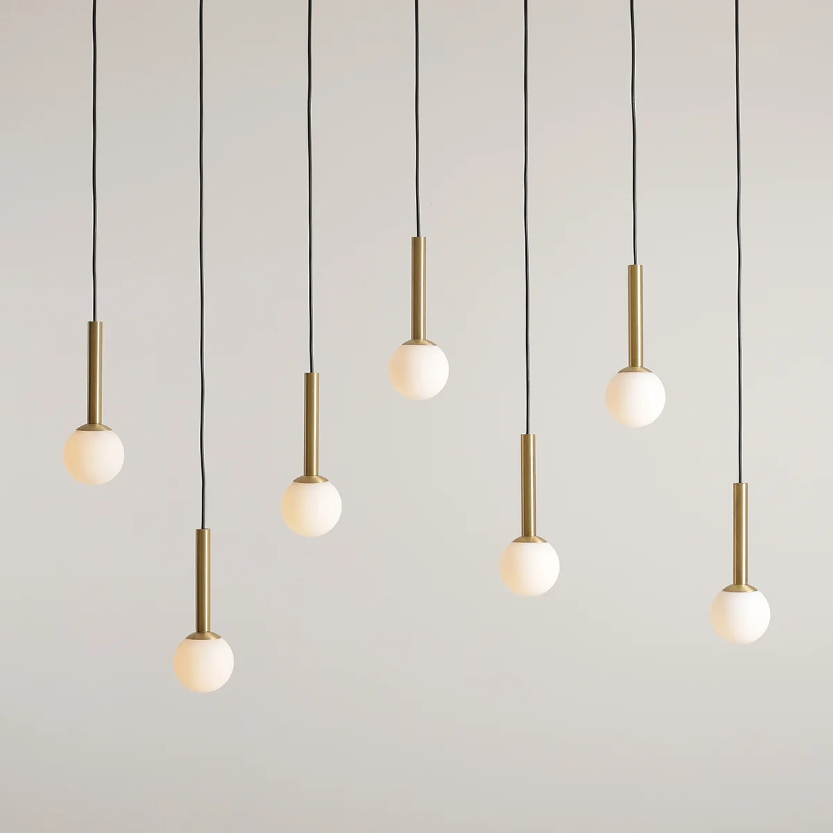 Lampa wisząca Riu, 7-punktowa, z czarnymi przewodami. Każda z siedmiu opraw posiada mosiężny uchwyt oraz okrągłą, matową szklaną kulę. Zawieszona w równych odstępach, tworzy nowoczesną aranżację na jasnym tle.