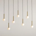Lampa wisząca Riu, 7-punktowa, z czarnymi przewodami. Każda z siedmiu opraw posiada mosiężny uchwyt oraz okrągłą, matową szklaną kulę. Zawieszona w równych odstępach, tworzy nowoczesną aranżację na jasnym tle.