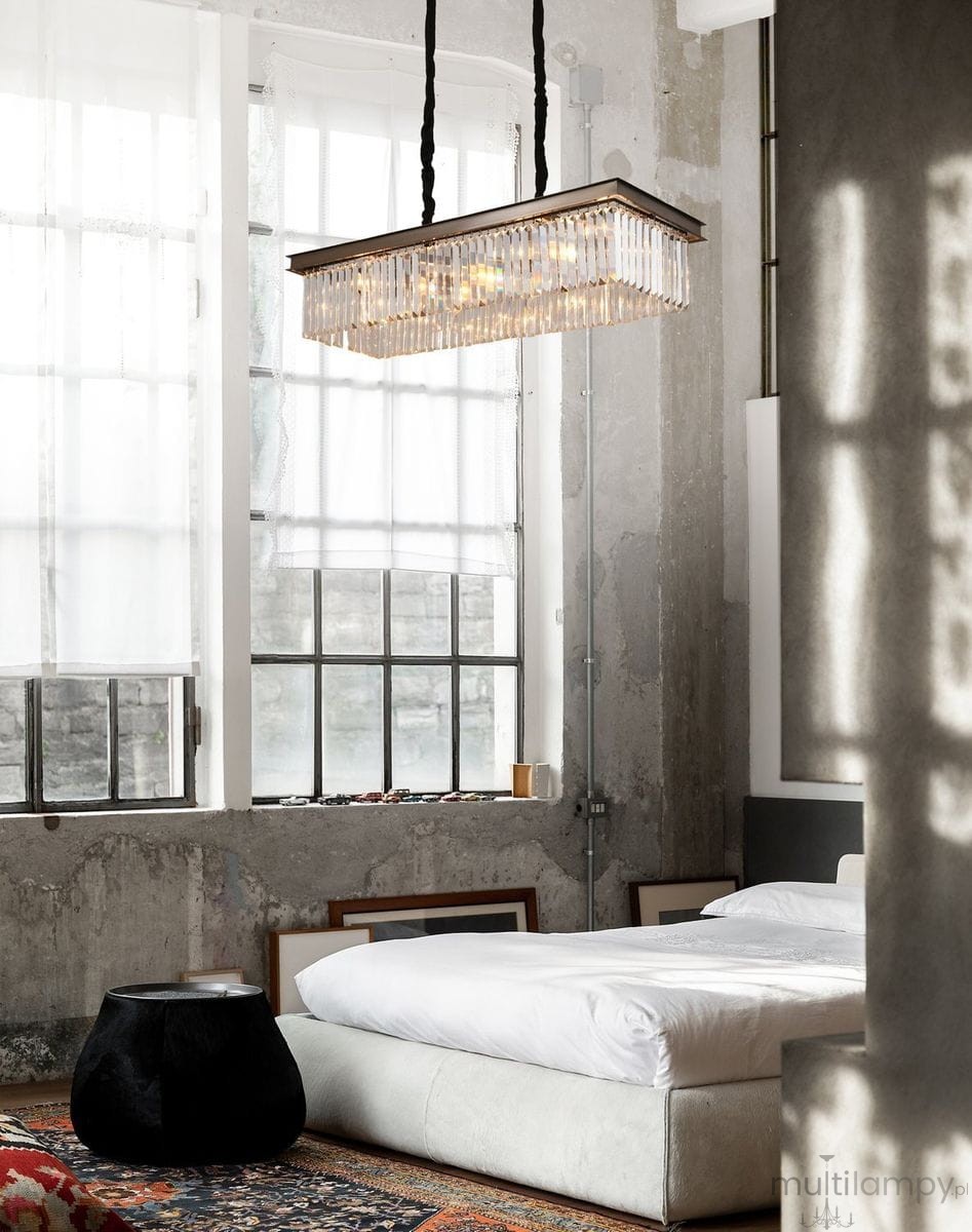 Lampa wisząca Sparkle w kolorze antracytowym, z 8 gniazdami E14, o prostokątnym kształcie. Zawieszona na czarnych przewodach, z dekoracyjnymi kryształkowymi elementami, w nowoczesnej aranżacji sypialni z jasnym łóżkiem i ciemnym stolikiem.