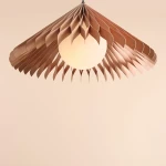 Lampa wisząca Nature Sun D58 z kloszem w kształcie rozłożonych liści w kolorze miedzianym, z okrągłą, białą żarówką E27. Zawieszona w centralnej części, na jednolitym, jasnym tle.