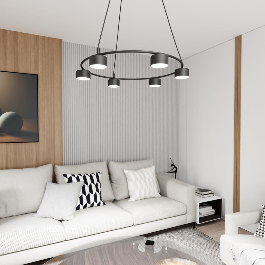 Lampa wisząca Starlit czarna z sześcioma oprawami GX53, umieszczona w nowoczesnym wnętrzu, z okrągłym metalowym stelażem. Widoczna nad kanapą z poduszkami w odcieniach szarości i bieli, na tle jasnej ściany z panelami i obrazem.