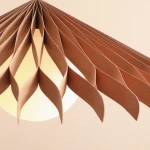 Lampa wisząca Nature Sun D69 z kloszem z tworzywa w kształcie falistych pasków w kolorze beżowym. Zawieszona pod kątem, oświetla dolną, okrągłą część. Idealna do nowoczesnych wnętrz.