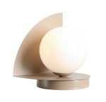 Beżowa lampa stołowa Loop z okrągłym, opalowym kloszem, osadzona na okrągłej podstawie. W tle widoczny asymetryczny, metalowy element w kształcie półokręgu. Lampa ma nowoczesny design, idealna do aranżacji wnętrz.