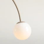 Lampa wisząca Una w kolorze beżowym z podwójnym źródłem światła E14. Okrągła, biała klosz wykonany z szkła, zawieszony na łukowatym, metalowym ramieniu. Tło jasne, neutralne.
