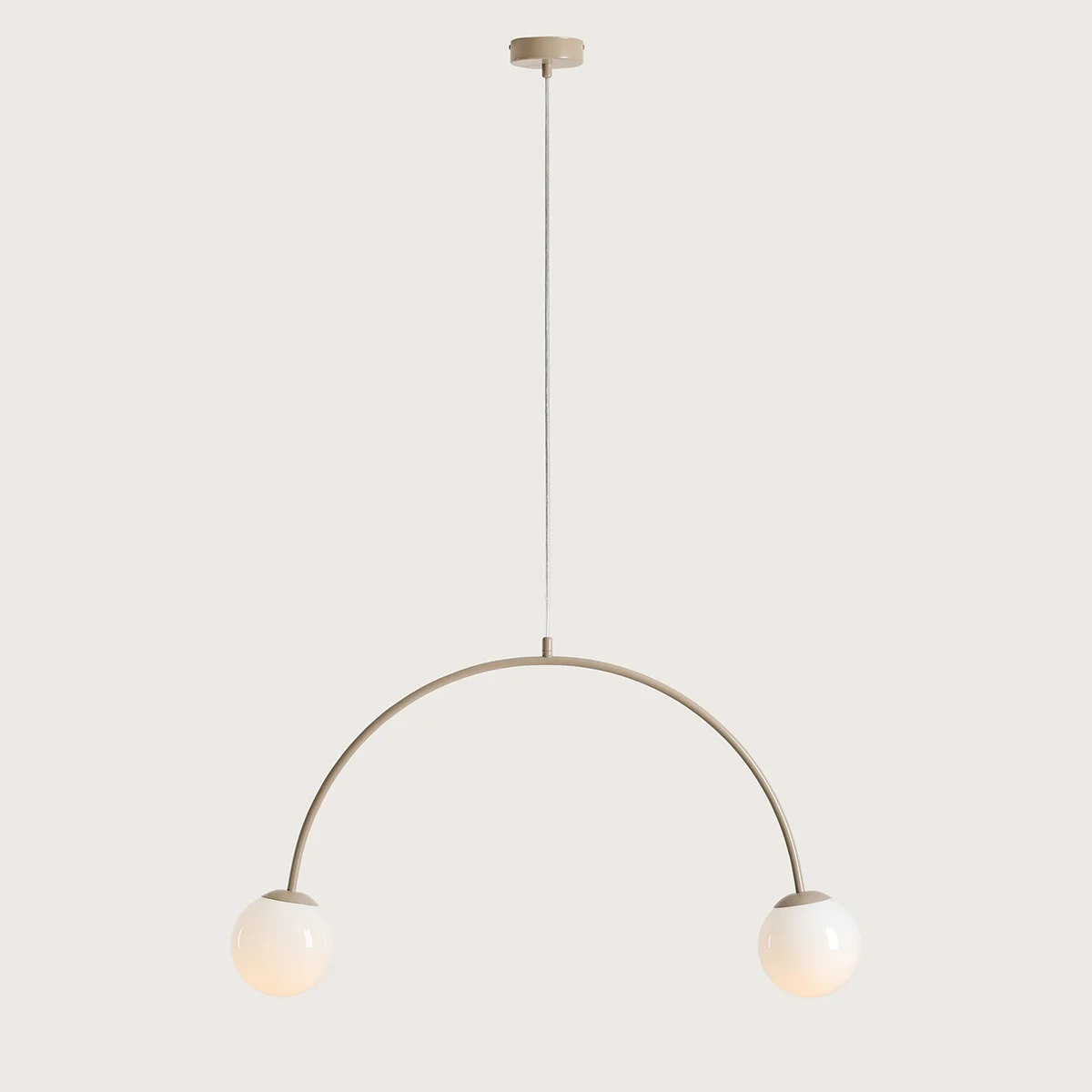 Lampa wisząca Una Beige z dwoma oprawami E14. Posiada łukowaty, beżowy metalowy stelaż z wiszącymi, okrągłymi kloszami w kolorze białym. Produkt zawieszony na białym przewodzie, z minimalistycznym mocowaniem do sufitu.