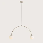Lampa wisząca Una Beige z dwoma oprawami E14. Posiada łukowaty, beżowy metalowy stelaż z wiszącymi, okrągłymi kloszami w kolorze białym. Produkt zawieszony na białym przewodzie, z minimalistycznym mocowaniem do sufitu.