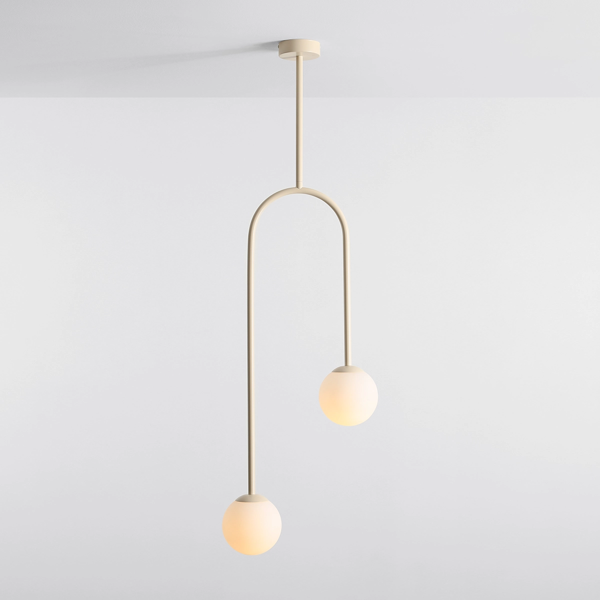 Lampa wisząca Nave 2xE14 w kolorze kremowym, złożona z dwóch okrągłych kloszy i cienkiego, łukowatego ramienia. Produkt zawieszony na długim, prostym przewodzie, umieszczony na jasnym tle.