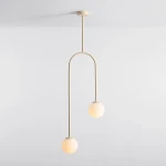 Lampa wisząca Nave 2xE14 w kolorze kremowym, złożona z dwóch okrągłych kloszy i cienkiego, łukowatego ramienia. Produkt zawieszony na długim, prostym przewodzie, umieszczony na jasnym tle.
