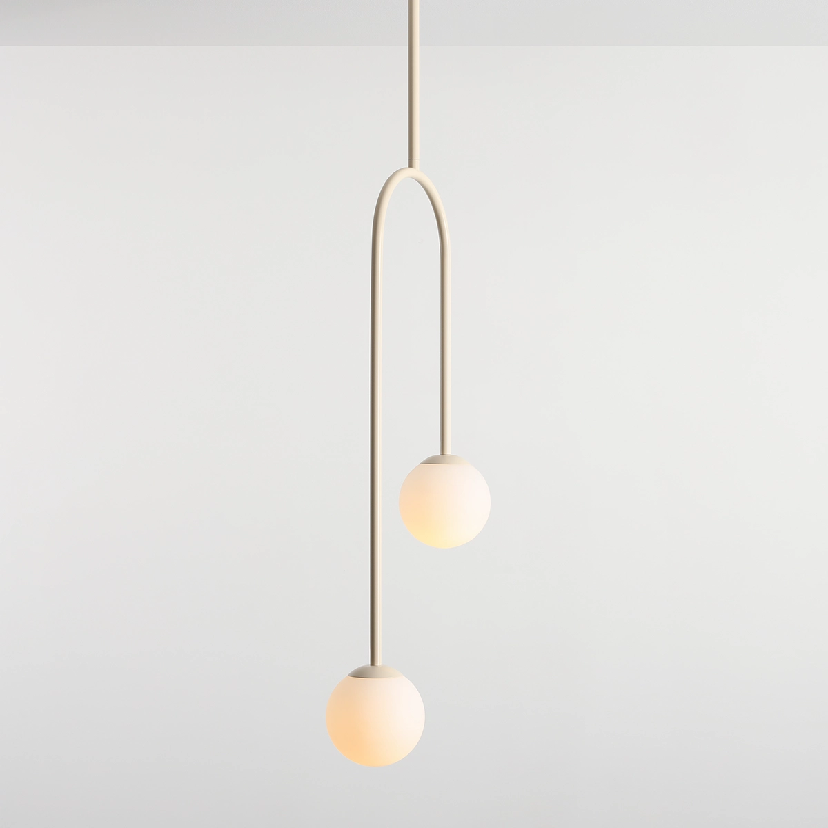 Lampa wisząca Nave w kolorze kremowym z dwoma okrągłymi kloszami. Klosze zawieszone na długim, łukowatym ramieniu, emitujące ciepłe światło. Prosta forma, idealna do nowoczesnych wnętrz, umieszczona na jasnym tle.