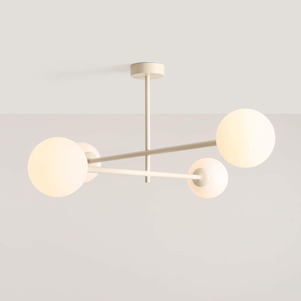 Kremowa lampa sufitowa Pinne z czterema oprawami E14, zbudowana z metalowych ramion i okrągłych kloszy w kolorze białym. Ujęcie z dołu, pokazujące lampę wiszącą na prostym, okrągłym mocowaniu. Tło jasne, minimalistyczne.