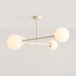 Kremowa lampa sufitowa Pinne z czterema oprawami E14, zbudowana z metalowych ramion i okrągłych kloszy w kolorze białym. Ujęcie z dołu, pokazujące lampę wiszącą na prostym, okrągłym mocowaniu. Tło jasne, minimalistyczne.