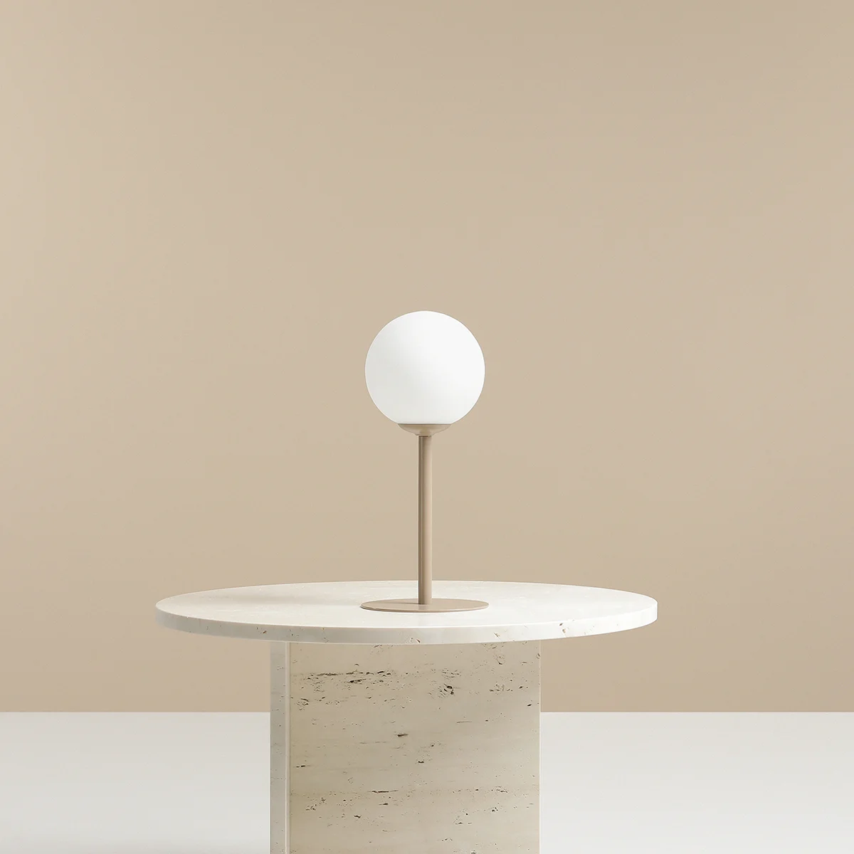 Beżowa lampa stołowa Pinne z okrągłą białą kloszem, umieszczona na okrągłej podstawie. Produkt stoi na jasnym stole w minimalistycznym otoczeniu, na jednolitym beżowym tle.