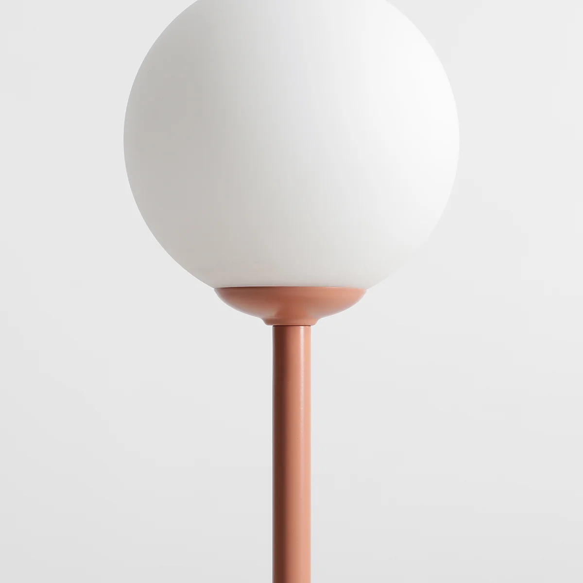 Lampa stołowa Pinne z koralowym stelażem i białym, okrągłym kloszem. Ujęcie z boku, pokazujące detale podstawy i klosza. Prosta, nowoczesna forma, idealna do aranżacji wnętrz.