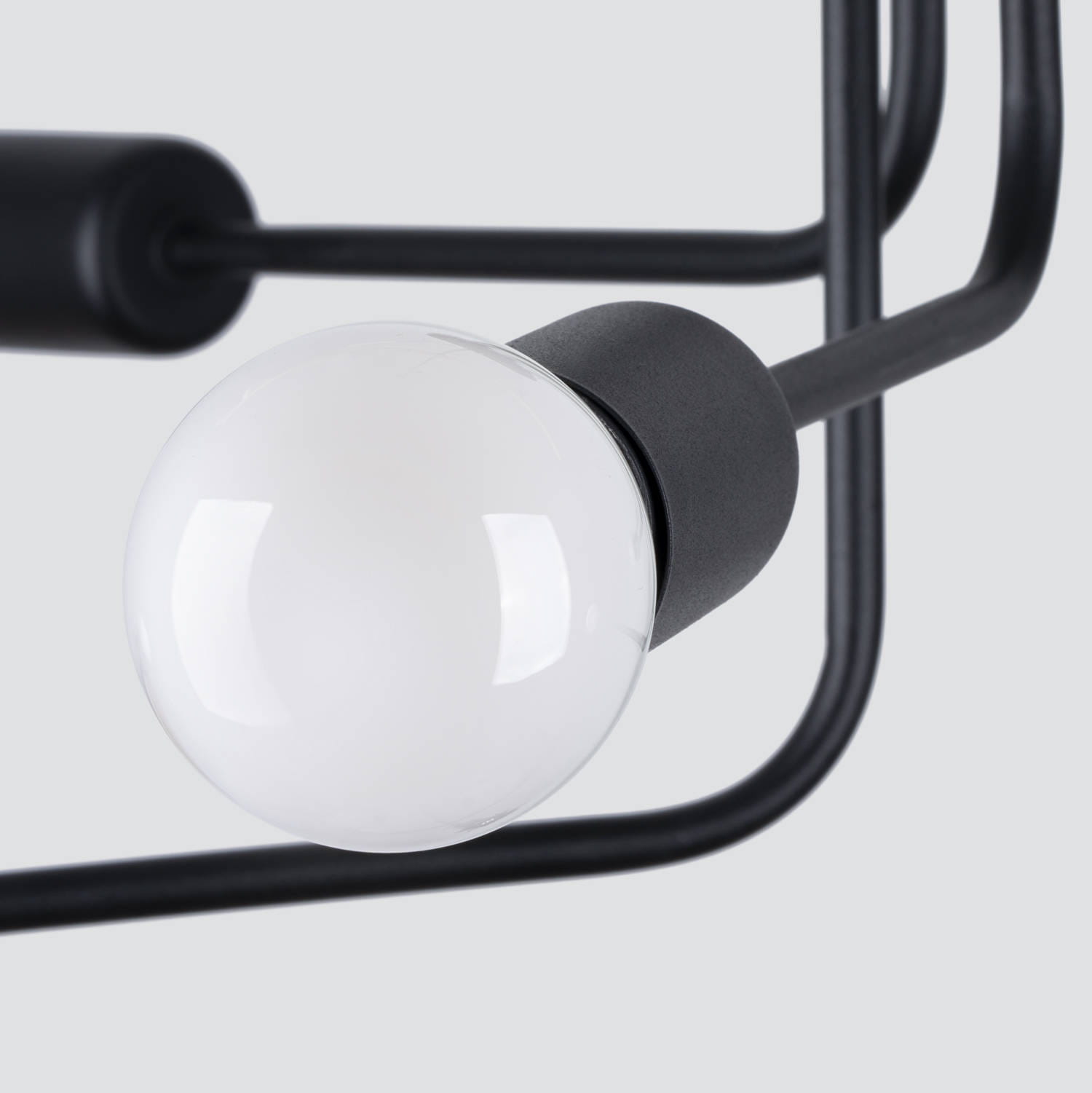 Czarna lampa sufitowa Norah z sześcioma gniazdami E27, z metalowym stelażem w minimalistycznym stylu. Widoczna kula lampy z białym kloszem, mocowana na czarnym elemencie. Ujęcie z bliska, ukazujące detal konstrukcji.