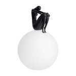 Lampa stołowa Woman-2 z czarną figurką kobiety siedzącej na białej, okrągłej podstawie. Figurka ma gładką, matową powierzchnię, a całość ma nowoczesny, minimalistyczny design. Idealna do stylowych wnętrz.