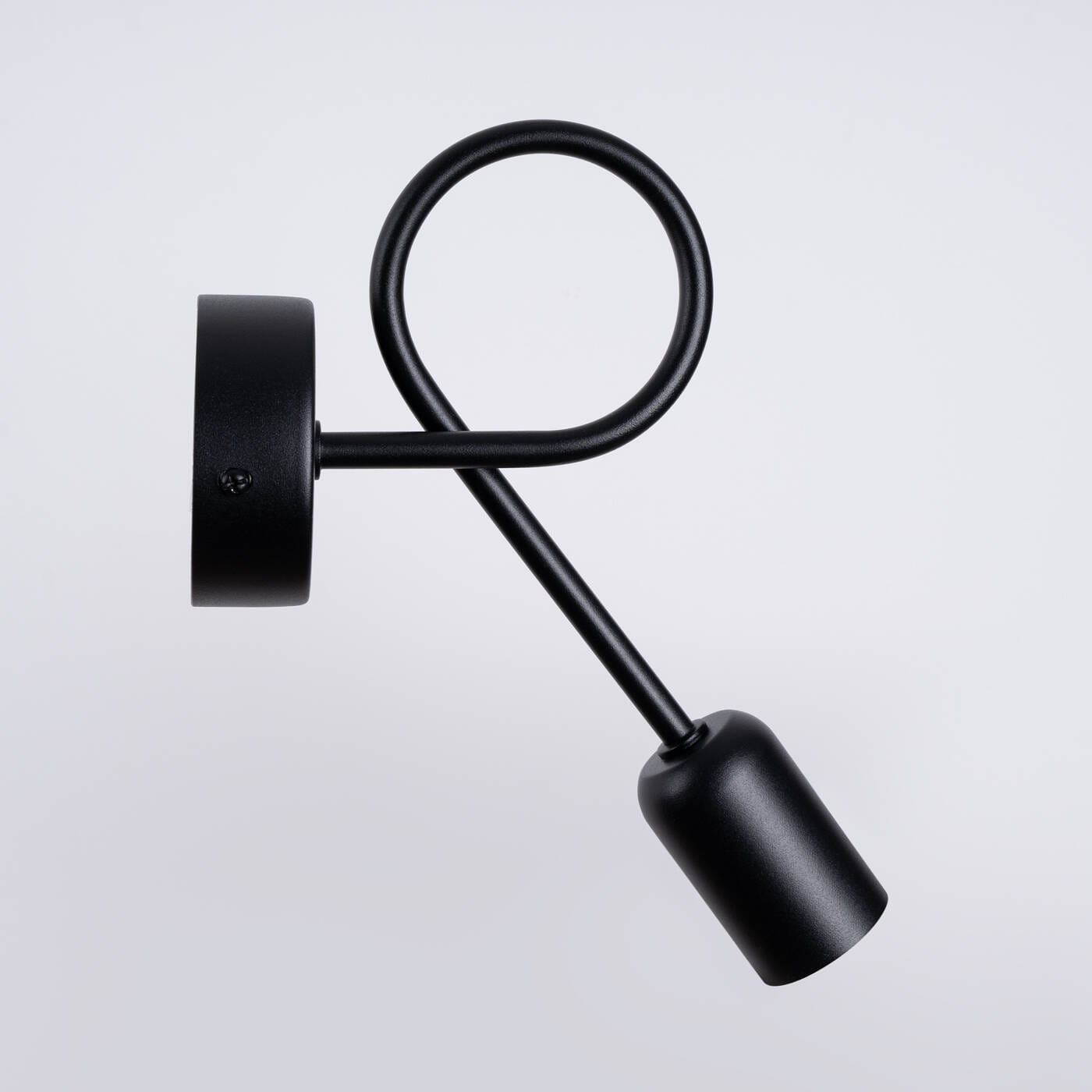 Kinkiet Supeł 1xE27 w kolorze czarnym, z okrągłą podstawą i zakrzywionym ramieniem. Lampa ma minimalistyczny design, z oprawą na żarówkę w formie cylindrycznej, zamontowaną na długim, cienkim ramieniu. Tło białe.