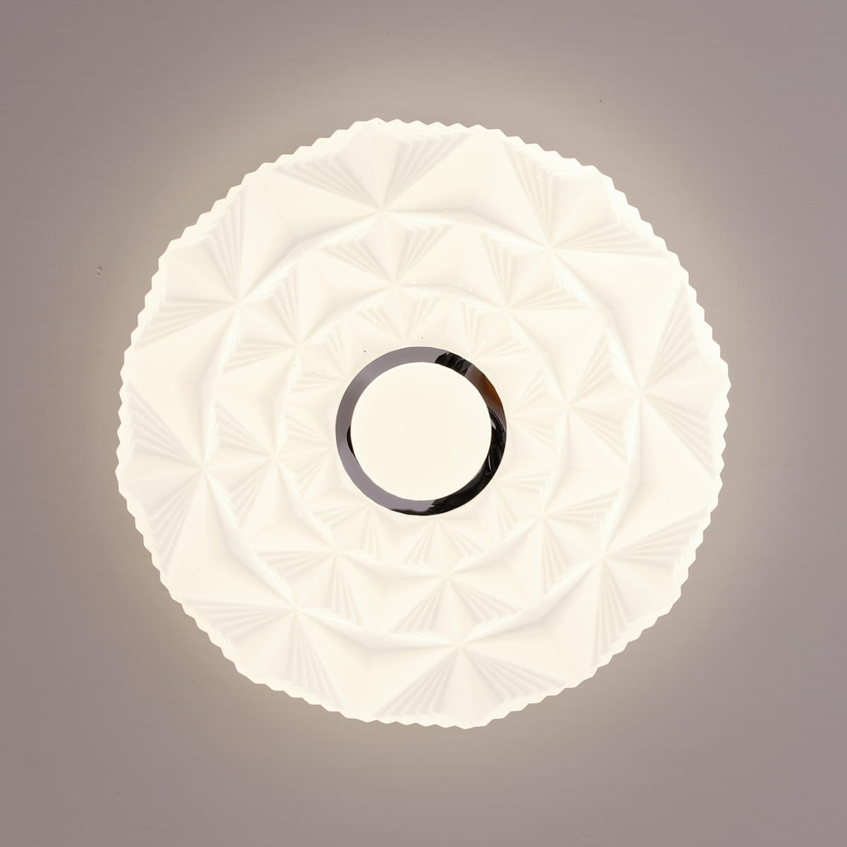 Plafon Kelmi D27 w kolorze białym i srebrnym, z LED 12W, 4000K. Okrągły kształt z dekoracyjną, teksturowaną powierzchnią. Widoczny centralny okrąg z metalicznym wykończeniem. Ujęcie z góry, na jasnym tle.