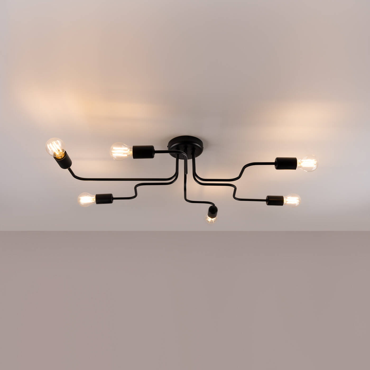 Czarna lampa sufitowa Vector z sześcioma ramionami na żarówki E27. Ujęcie z dołu, pokazujące rozchodzące się ramiona i żarówki, które emitują ciepłe światło. Prosty, nowoczesny design, montowana na suficie.