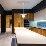 Lampa wisząca Robin D25 w kolorze białym z kloszem w kształcie okręgu, zawieszona na cienkim przewodzie, umieszczona nad białym blatem kuchennym, w nowoczesnym wnętrzu z drewnianymi szafkami i czarnymi akcentami.