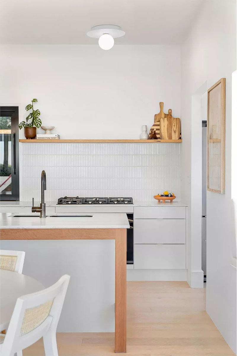 Lampa sufitowa Robin D25 w kolorze białym z oprawą na jedną żarówkę G9. Montowana na suficie, z okrągłym kloszem, w nowoczesnej kuchni z jasnymi meblami i drewnianym blatem. W tle widoczne akcesoria kuchenne i roślina doniczkowa.