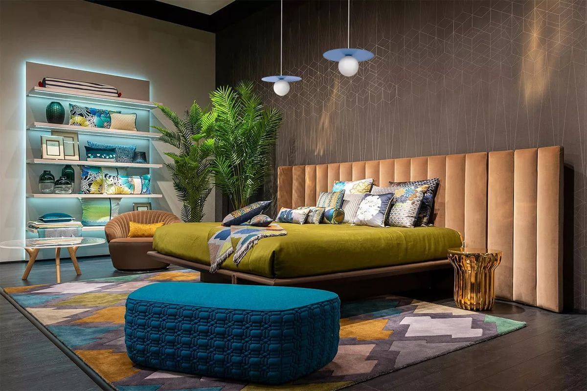 Lampa wisząca Robin D25 z jednym źródłem światła G9, w kolorze niebieskim i białym. Zawieszona w sypialni, na tle ciemnej ściany, obok ozdobnych poduszek i roślin. Kąt ujęcia frontalny, ukazujący również meble i dekoracje w otoczeniu.